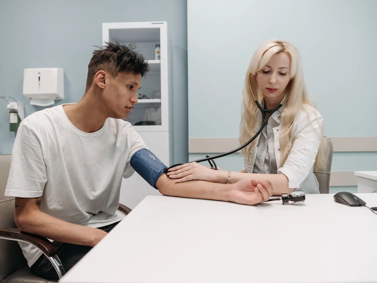 A clinician checks a seated man's blood pressure with a manual cuff.